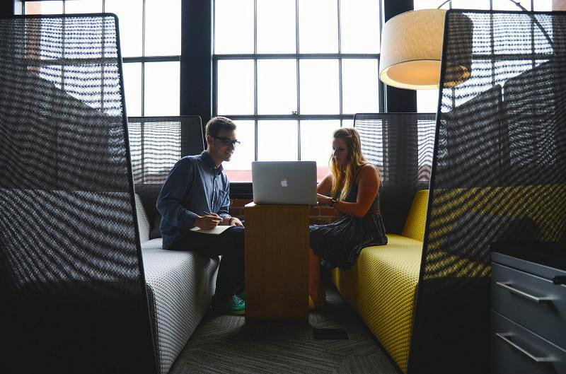 A man and a woman sitting down across from eachother working together on a Macbook